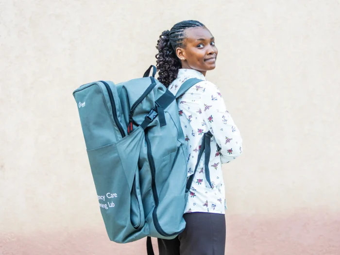 A woman facing away from the camera is seen wearing the Emergency Care Learning Lab backpack, looking over her shoulder towards the camera visibly smiling.